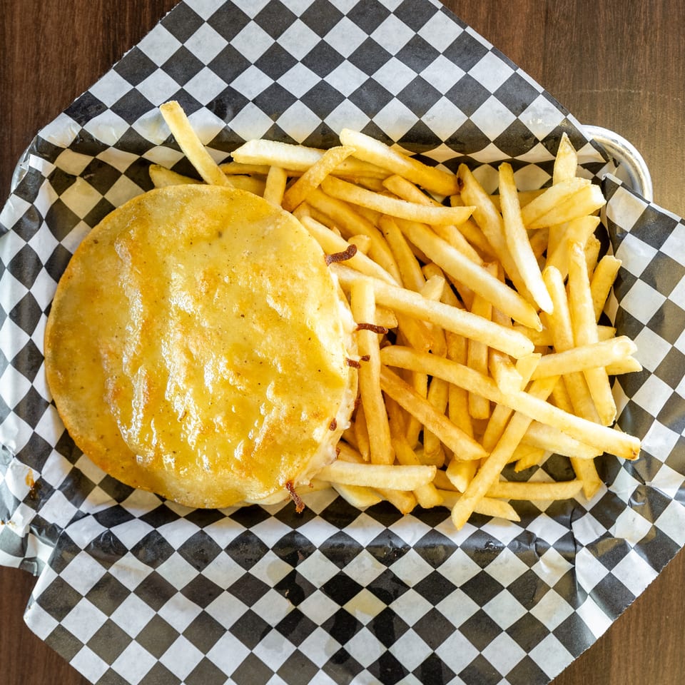Cheesy burger patty and golden french fries in a checkered paper-lined basket on a wooden table.