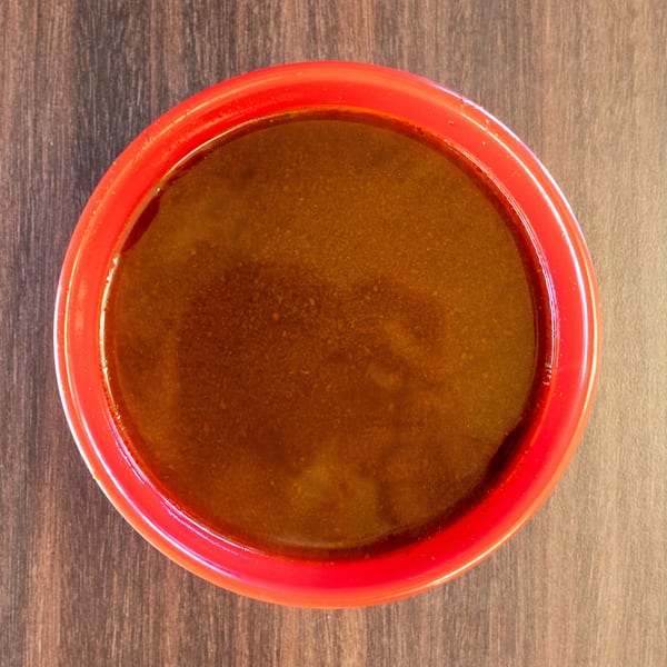 Overhead view of a red bowl filled with dark brown sauce on a wooden table.