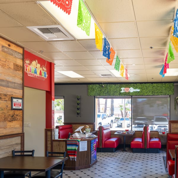 Interior of a Mexican restaurant with red booths, patterned floor, and colorful papel picado banners.