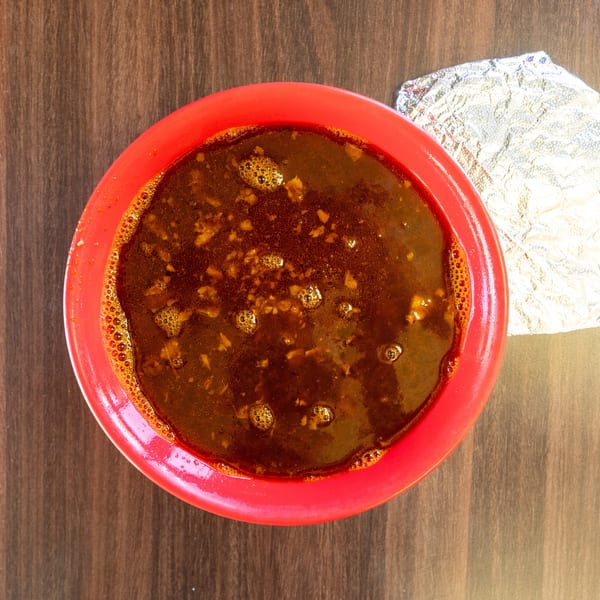 Overhead view of a red bowl filled with a dark, chunky sauce, next to crumpled foil.