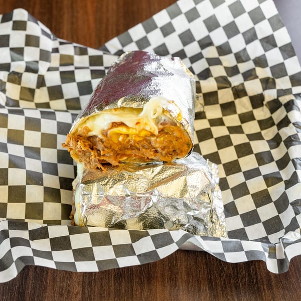 A large burrito, cut in half, wrapped in foil and checkered paper, revealing its meaty, cheesy filling.