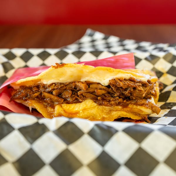 A cheesy arepa filled with shredded beef and onions, served in checkered paper.