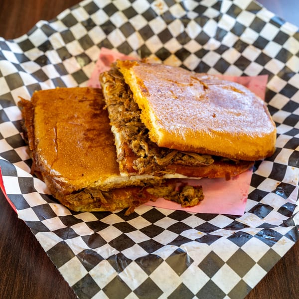 A Cuban sandwich with shredded meat, cheese, and pickles on toasted bread, served in a red basket.