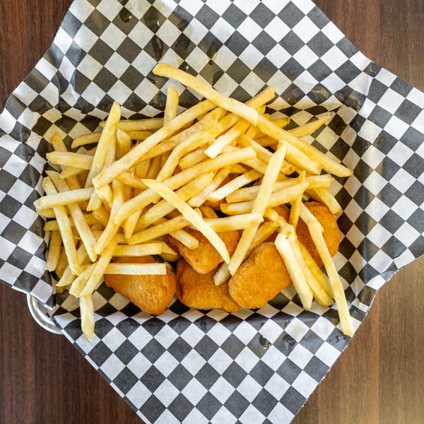 Golden french fries and chicken nuggets in a checkered paper-lined basket on a wooden table.