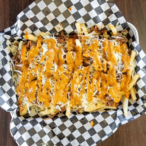 Loaded fries with shredded meat, white cheese, and orange sauce in a checkered paper-lined basket.