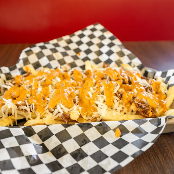 Loaded fries with shredded cheese, pulled pork, and orange sauce in a checkered paper-lined basket.