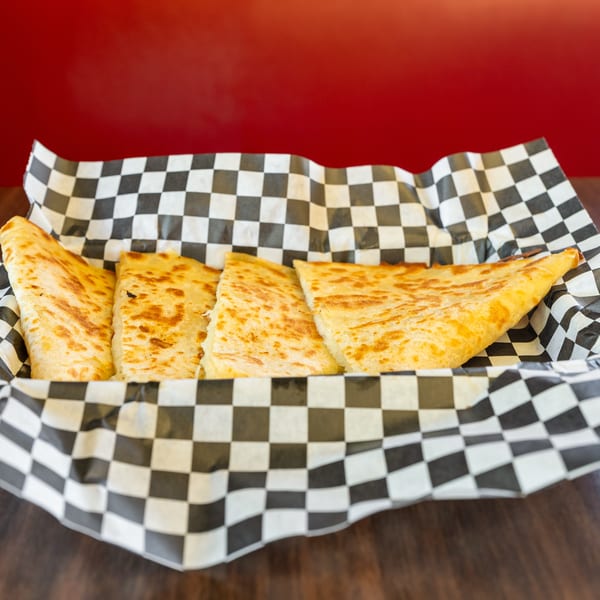 Four cheese quesadilla slices in a checkered paper-lined basket on a wooden table with a red background.
