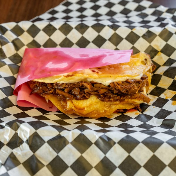 A cheesy quesadilla filled with shredded meat, wrapped in pink paper and black-and-white checkered paper.