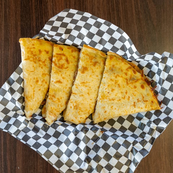 Four golden-brown quesadilla slices with melted cheese and filling, served in a black and white checkered paper.