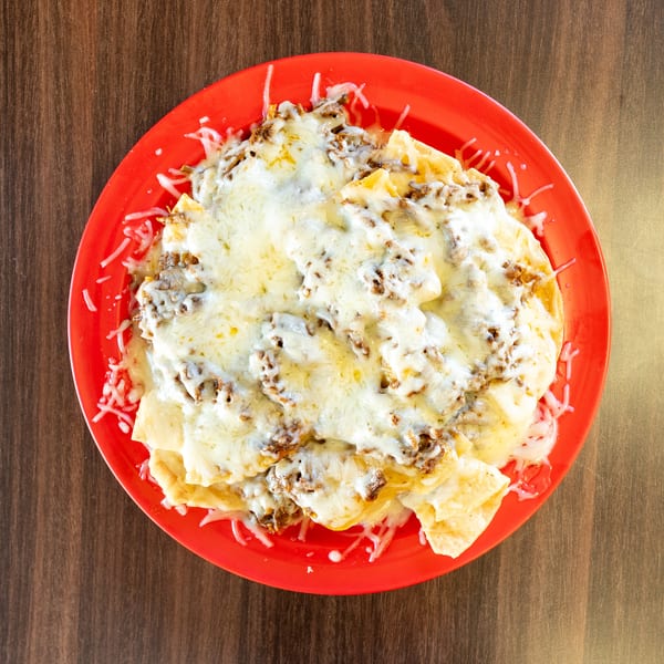 Overhead view of a red plate piled high with cheesy beef nachos on a wooden table.
