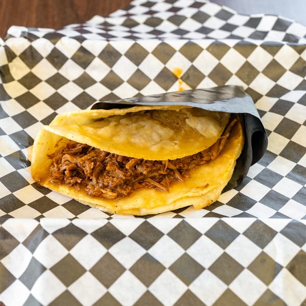 A golden-brown quesadilla filled with shredded meat, served in black and white checkered paper.